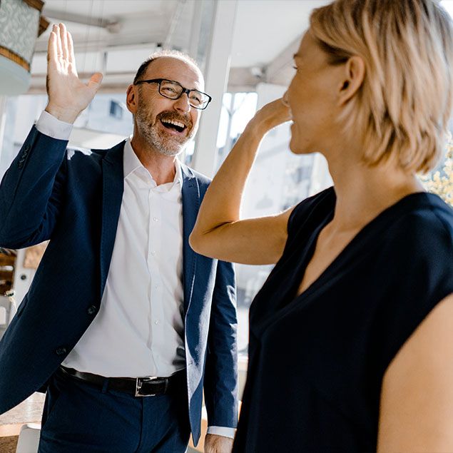 Mann und Frau im Business-Outfit geben sich ein High-Five und lachen.